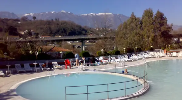 Piscine termali con lettini e ombrelloni, montagne innevate sullo sfondo. Un'oasi di relax per godersi le contursi terme gratis.