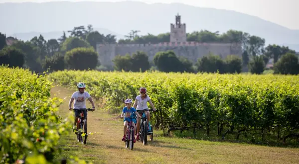 Famiglia in bicicletta tra i vigneti, con un castello sullo sfondo, lungo la ciclovia Bergamo Brescia.