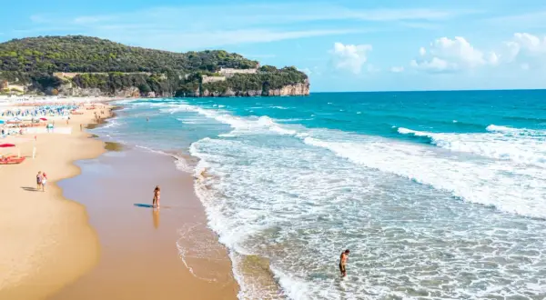 Spiaggia dorata con onde azzurre, scogliere verdi e un castello in cima. Perfetto per chi cerca il mare nel Lazio dove andare.