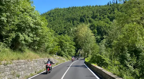 Motociclisti sfrecciano su strade panoramiche dell'Emilia Romagna, tra colline verdi e cielo azzurro.
