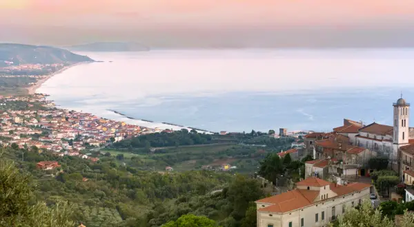 Vista panoramica di un borgo costiero nel Cilento, con case arroccate su una collina che scende verso il mare azzurro.