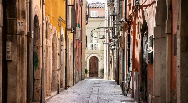 Un vicolo stretto nel chia centro storico, con edifici colorati, archi in pietra e un'antica porta in legno in fondo.