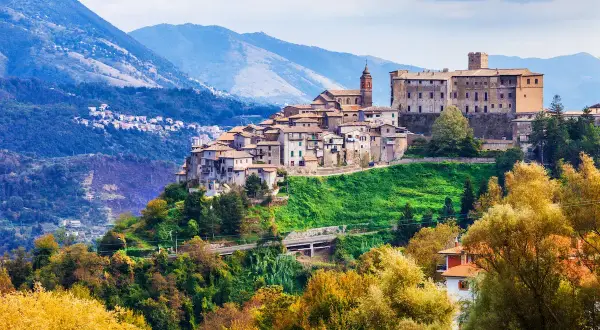Borgo medievale su una collina verde, con montagne sullo sfondo. Un gioiello di montagna vicino Roma, con case antiche e un castello imponente.