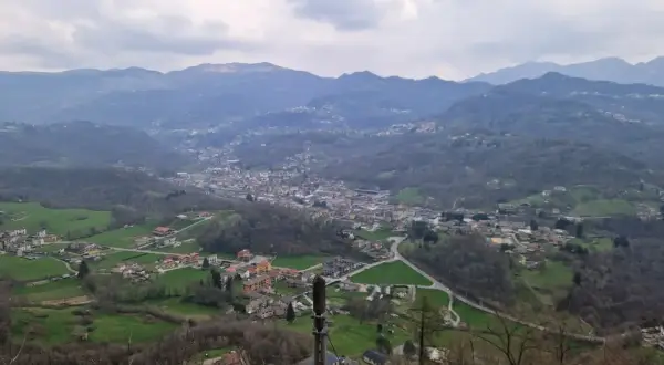 Panoramica della valle Imagna con case sparse tra colline verdi e montagne nebbiose sullo sfondo.