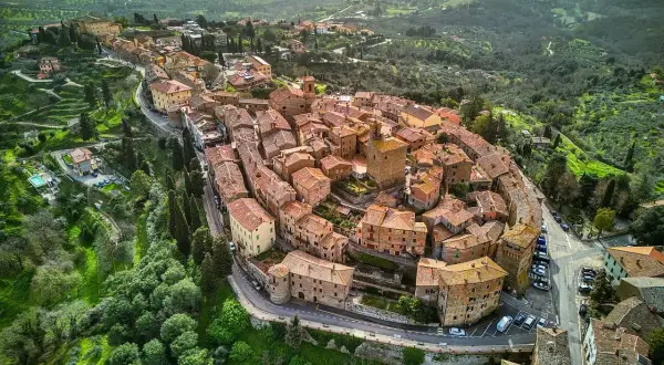 Vista aerea del borgo Panicale in Umbria, con le sue case in pietra e tetti rossi che si aggrappano alla collina, circondato da verdi colline.