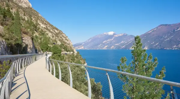Una moderna ciclabile a picco sul lago, con montagne sullo sfondo. Potrebbe essere la ciclabile più bella d'Italia.