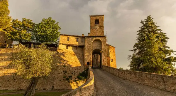Antica porta di Montegridolfo cosa vedere: un borgo medievale con torre campanaria e vicoli acciottolati, immerso nel verde.