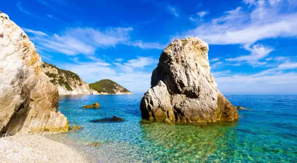 Scogliera imponente su una spiaggia di ciottoli, mare cristallino e isole verdi all'orizzonte. Una splendida località di mare tra Lazio e Toscana.