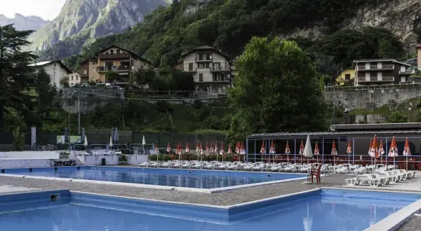 Piscine azzurre a Sant'Omobono Terme, con montagne verdi sullo sfondo e case arroccate.