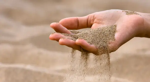Mano che lascia cadere sabbia bianca, come il tempo che scorre via.
