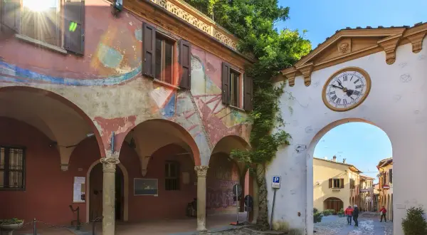 Un arco con orologio conduce a una strada acciottolata, un invito a scoprire i borghi da visitare vicino a Forlì.