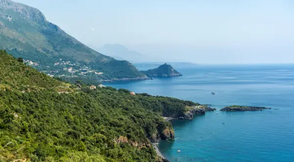 Costa verde e blu intenso del policastro mare, con case sparse tra la vegetazione e montagne sullo sfondo.