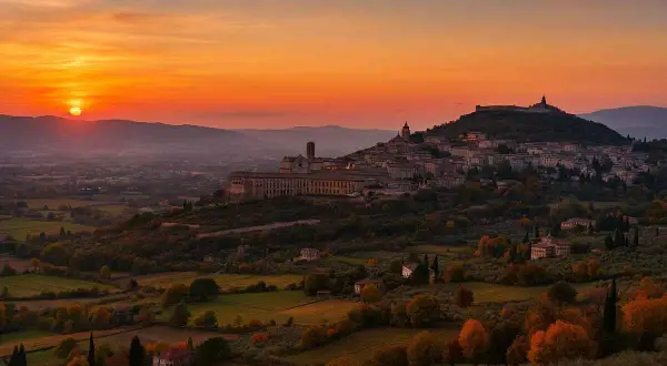 Tramonto infuocato su una città dell'Umbria arroccata su una collina, con uliveti e campi dorati.