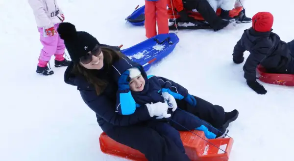 Mamma e bambino felici sciano in Abruzzo con slittino. Altri bambini giocano sulla neve.