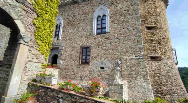 Antica dimora a Compiano, Parma, con mura in pietra, edera rampicante, fiori e una statua.