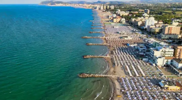 Vista aerea di una spiaggia affollata con ombrelloni colorati e il mare azzurro, tipica di una città riviera romagnola.