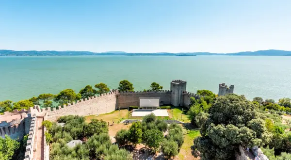 Vista dall'alto di un castello con un cinema all'aperto, circondato da ulivi e affacciato sul lago Trasimeno, uno dei borghi vicino Castiglione del Lago.