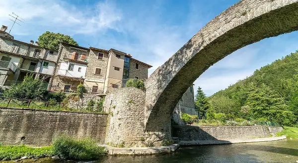 Antico ponte in pietra a schiena d'asino, con case aggrappate alla collina. Un scorcio suggestivo del portico di Romagna.