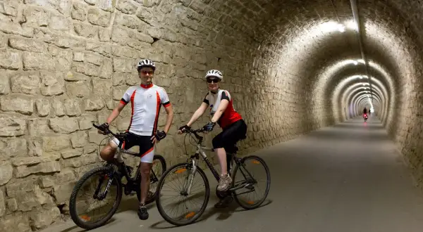 Coppia in bicicletta nel tunnel del **parenzana tracciato**, un percorso suggestivo tra storia e natura.