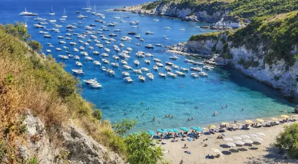 Baia con acque cristalline e numerose barche ormeggiate. La spiaggia di sabbia dorata è animata da ombrelloni e bagnanti. Un vero paradiso tra le spiagge di Ponza.
