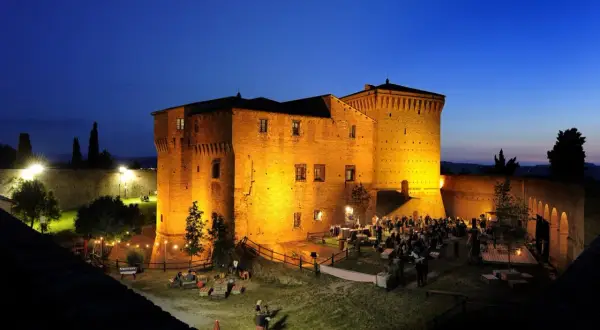 Rocca Malatestiana illuminata di sera, con persone che socializzano e godono dell'atmosfera. Un luogo suggestivo da scoprire tra le cose da vedere a Cesena.