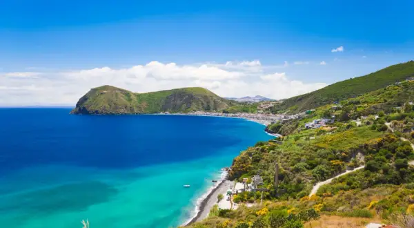 Splendido mare di Lipari con acque cristalline che lambiscono una costa verdeggiante e un borgo bianco.