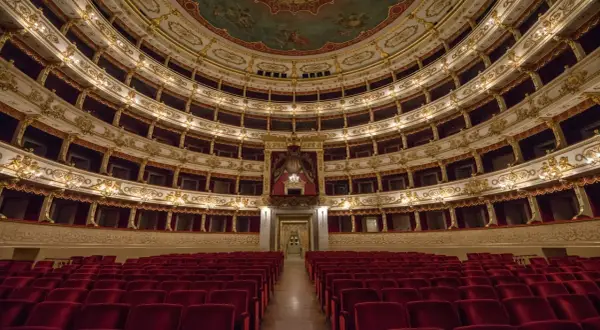 Interno di un teatro storico con file di poltrone rosse e palchi dorati. Un luogo da scoprire tra le cose da vedere a Parma gratis.