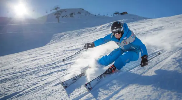 Sciatore in azione su una pista innevata, tipica delle località sciistiche Piemonte, con sole splendente e skilift sullo sfondo.