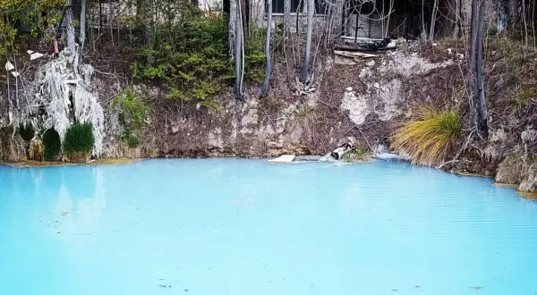 Acque azzurre e torbide delle terme di Cotilia, con vegetazione rigogliosa e rocce erose.