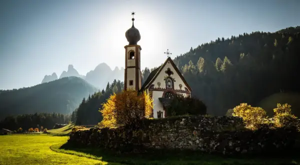 Chiesa di San Giovanni in Ranui, incastonata nel **Val di Funes**, con le Dolomiti sullo sfondo illuminate dal sole.