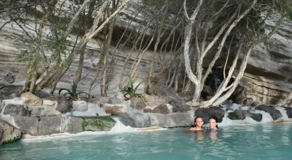 Due bambine si godono le terme libere di Ischia, immerse in acque turchesi tra rocce e vegetazione rigogliosa.