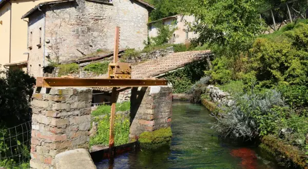Un canale d'acqua cristallina attraversa un borgo antico, ricordando la Venezia dell'Umbria. Edifici in pietra e vegetazione rigogliosa incorniciano questo scorcio pittoresco.