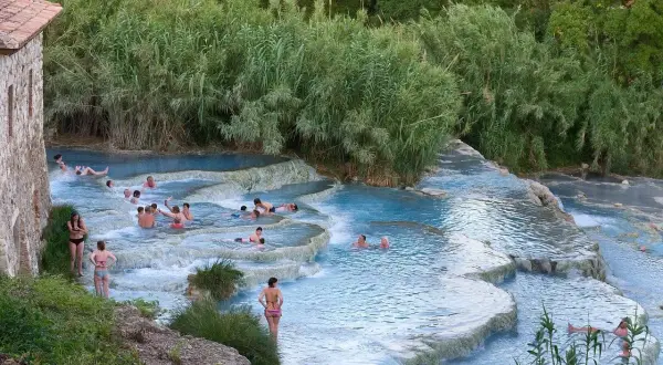 Persone si rilassano nelle cascate termali naturali. Un luogo ideale per scoprire le terme Pavia prezzi.