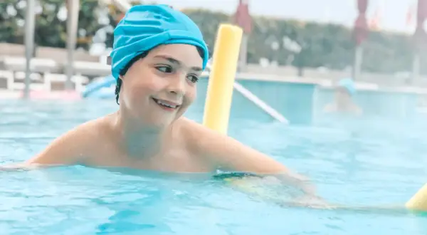 Un bambino sorridente con cuffia azzurra si diverte in piscina, un'ottima opzione per le terme Sirmione bambini.
