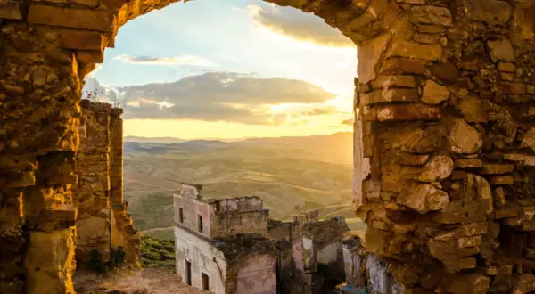Rovine di **paesi abbandonati in Italia** illuminate dal tramonto, con colline ondulate all'orizzonte.