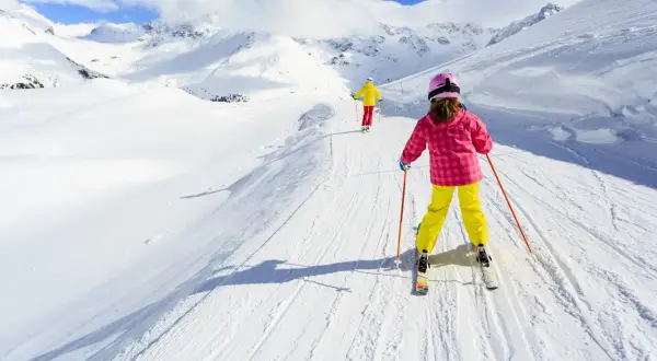 Bambini imparano a sciare su piste da sci per principianti, con montagne innevate sullo sfondo.