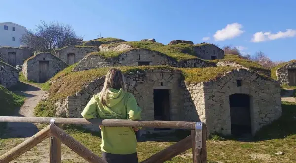 Pietragalla cosa vedere: antiche case-grotta scavate nella collina, con una donna che le osserva. Un luogo suggestivo da esplorare.