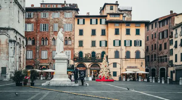La piazza di Lucca con la statua bianca, edifici storici e un albero di Natale decorato.