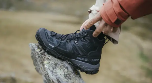 Come scegliere scarpe da trekking: un piede indossa uno scarpone nero Mammut su una roccia.