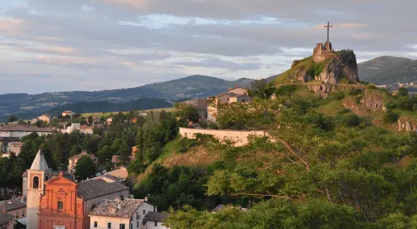Panoramica di Pennabilli, Rimini, con la chiesa e la rocca con la croce che domina il paesaggio collinare al tramonto.