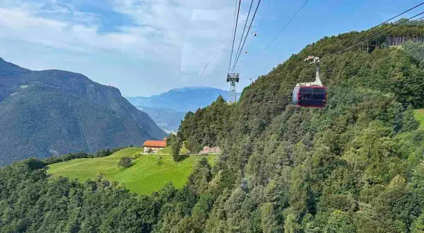 Cabina del trenino del Renon in viaggio tra boschi e montagne, con una casa su un prato verde. Cosa vedere in questo paesaggio mozzafiato.
