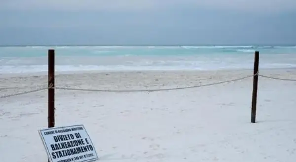 Spiagge bianche deserte con mare turchese. Un cartello vieta balneazione e stazionamento.