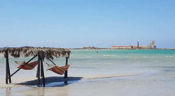 Amache colorate sotto un tetto di paglia, con il mare turchese e antichi edifici all'orizzonte. Un angolo di paradiso a San Teodoro, spiaggia rosa.