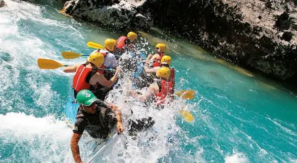 Un gruppo di persone si diverte con il rafting in Emilia Romagna, pagaiando tra spruzzi d'acqua cristallina e rocce.