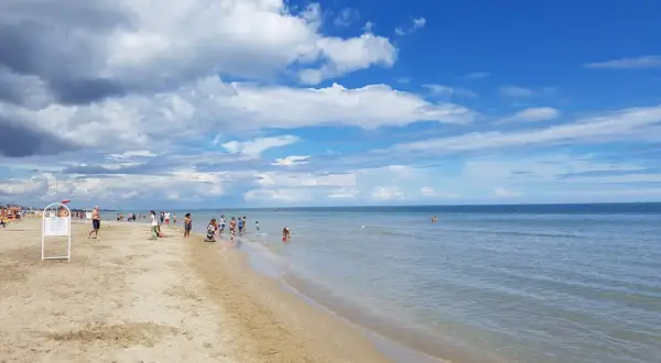 Giornata di sole e nuvole sul mare di Riccione. Bambini giocano sulla battigia mentre adulti passeggiano sulla sabbia dorata.