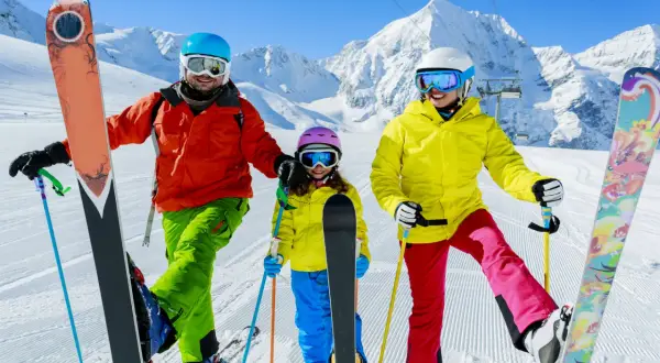 Famiglia felice sulle piste innevate, pronta dove imparare a sciare. Montagne maestose e cielo azzurro fanno da sfondo a questa avventura.