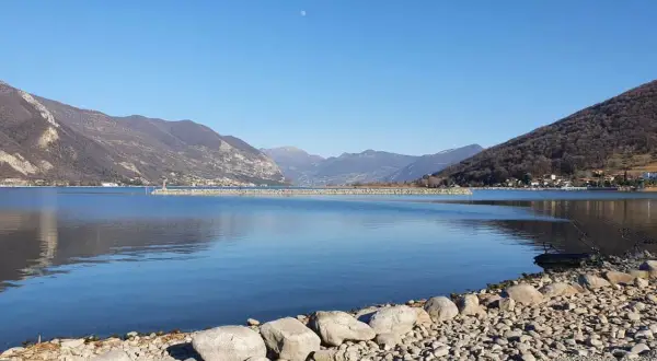 Calm lake with mountains in the background and a rocky shore in the foreground.