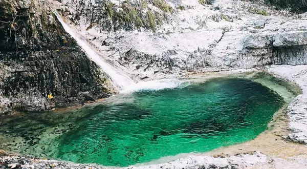 Cascata e pozza smeraldo nella valle del Mis, con rocce bianche e vegetazione.