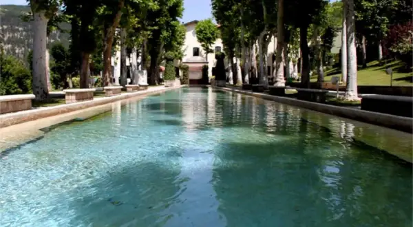 Vasca d'acqua cristallina con alberi secolari e un edificio sullo sfondo, un'oasi di pace a Caramanico Terme.