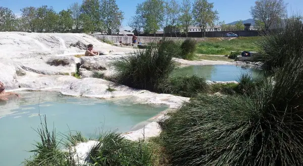 Persone rilassate nelle piscine naturali di acqua termale, un'oasi di pace tra rocce bianche e vegetazione rigogliosa, un vero paradiso per chi cerca le piscine carletti.